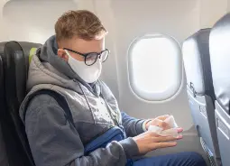 Junge mit Maske und Desinfektionstuch im Flugzeug Auf Klassenfahrt mit HEROLÉ: Ihre Sicherheit ist für uns das oberste Ziel.