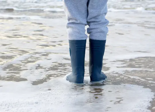 Auf Klassenfahrt mit HEROLÉ: Ein Jugendlicher in blauen Gummistiefeln am Nordseestrand.