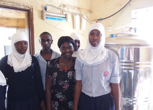 Afrikanische Schülergruppe vor der Trinkwasseraufbereitungsanlage des Projects myclimate in Uganda Auf Klassenfahrt mit HEROLÉ: Unterstützen Sie das Projekt "myclimate" und besichtigen Sie die Aufbereitungsanlage für Trinkwasser in Uganda