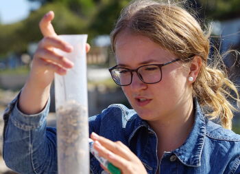 Schülerin untersucht Probe am Strand Auf Klassenfahrt mit HEROLÉ: Teil des Workshops ist die Untersuchung von Sedimentproben