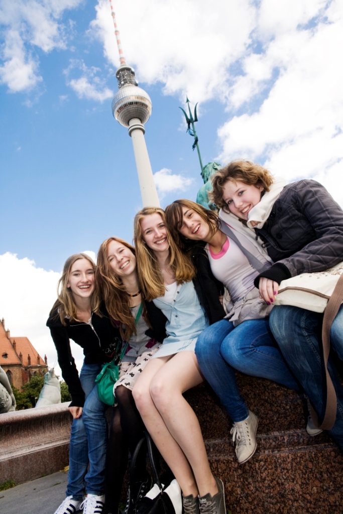 Schülerinnen sitzen auf Klassenfahrt vor dem Fernsehturm in Berlin