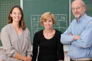 Drei Lehrkräfte vor einer Tafel im Klassenzimmer.