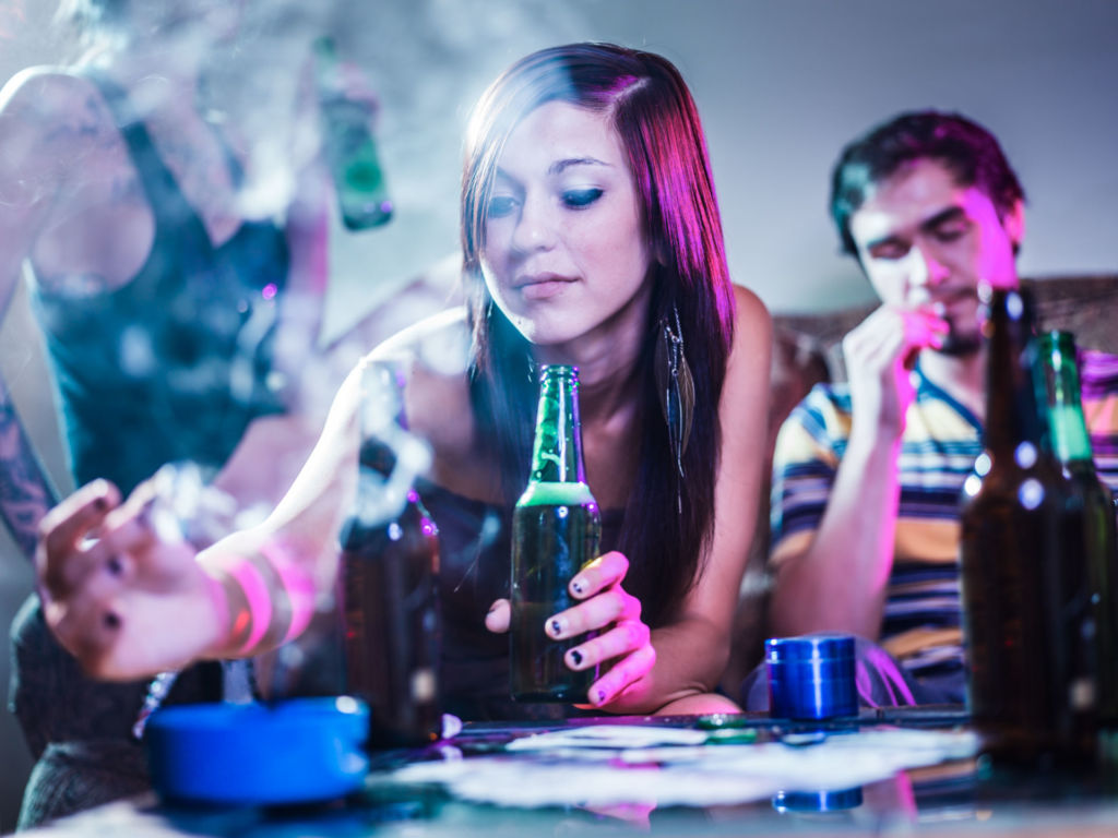 Eine Jugendliche die Alkohol trinkt, drückt eine Zigarette aus.