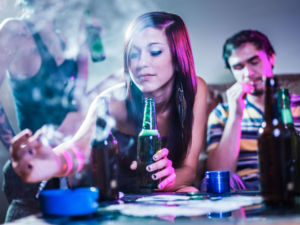 Eine Jugendliche die Alkohol trinkt, drückt eine Zigarette aus.