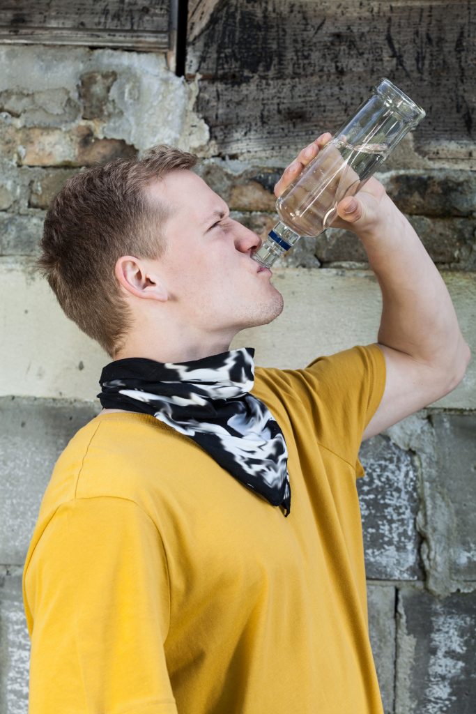 Junge hält eine Flasche mit Alkohol in der Hand und trinkt diesen