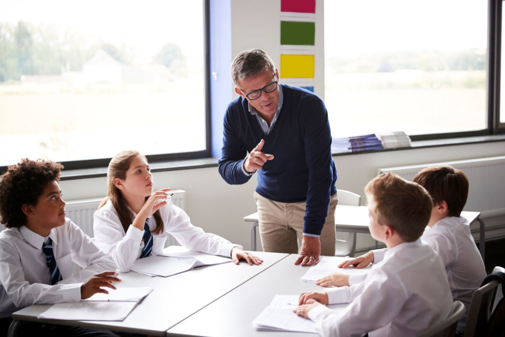 Ein Lehrer erklärt vier Schülern einen Sachverhalt im Rahmen einer Gruppenarbeit (© Shutterstock Bild-ID: 1195671607)