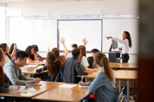 Eine Lehrerin am Whiteboard nimmt nach Meldung einen Schüler dran.