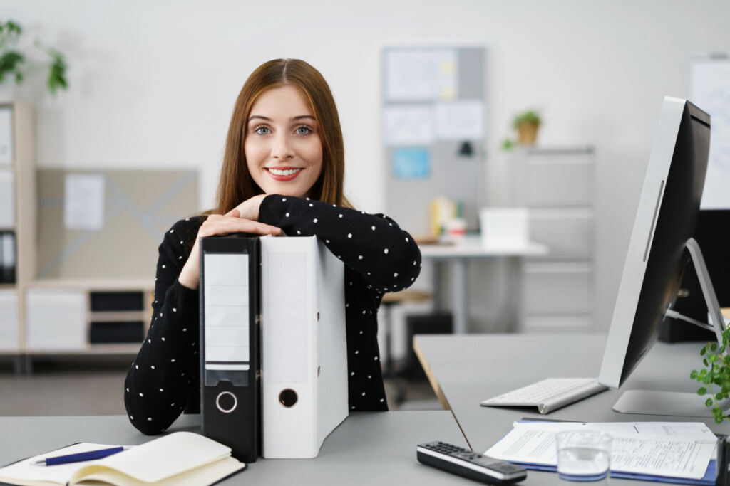 Junge Frau sitzt zu Hause am Schreibtisch vor ihren Aktenordnern und vor dem Computer. Wie Sie Eltern von einer Klassenfahrt begeistern können, erfahren Sie im HEROLÉ Ratgeber.