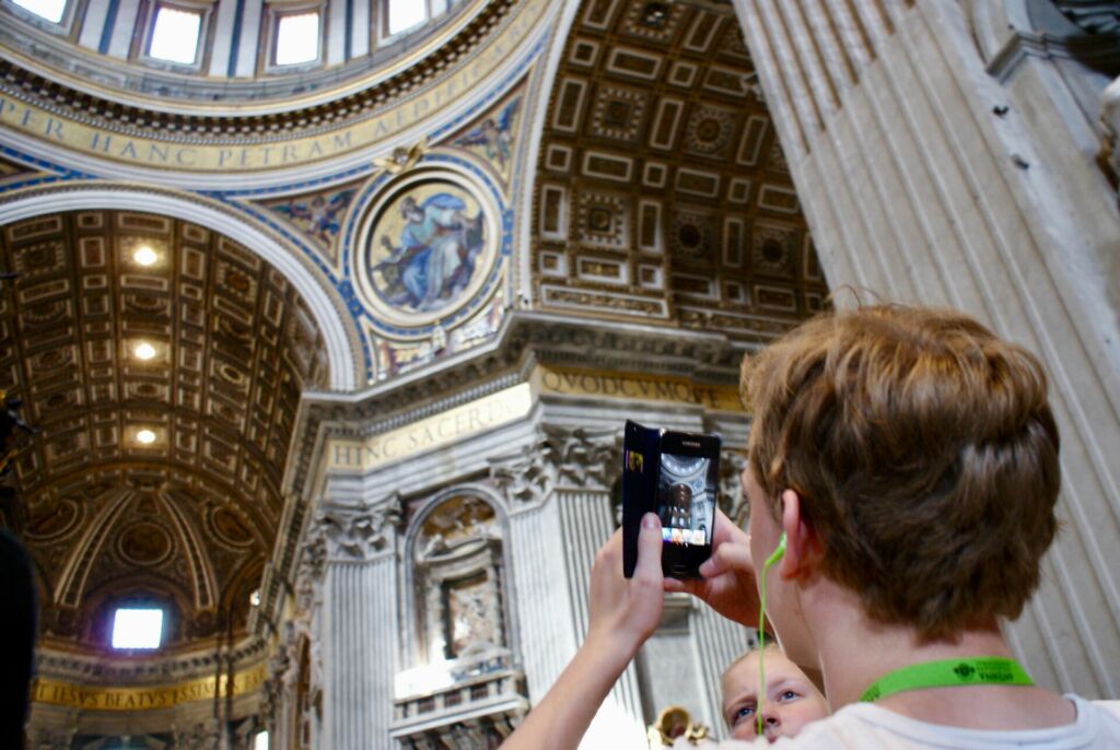 Schüler macht mit seinem Smartphone ein Bild der Kuppel des Petersdoms im Vatikan.