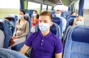 Schüler mit Abstand und Maske im Reisebus auf Klassenfahrt.