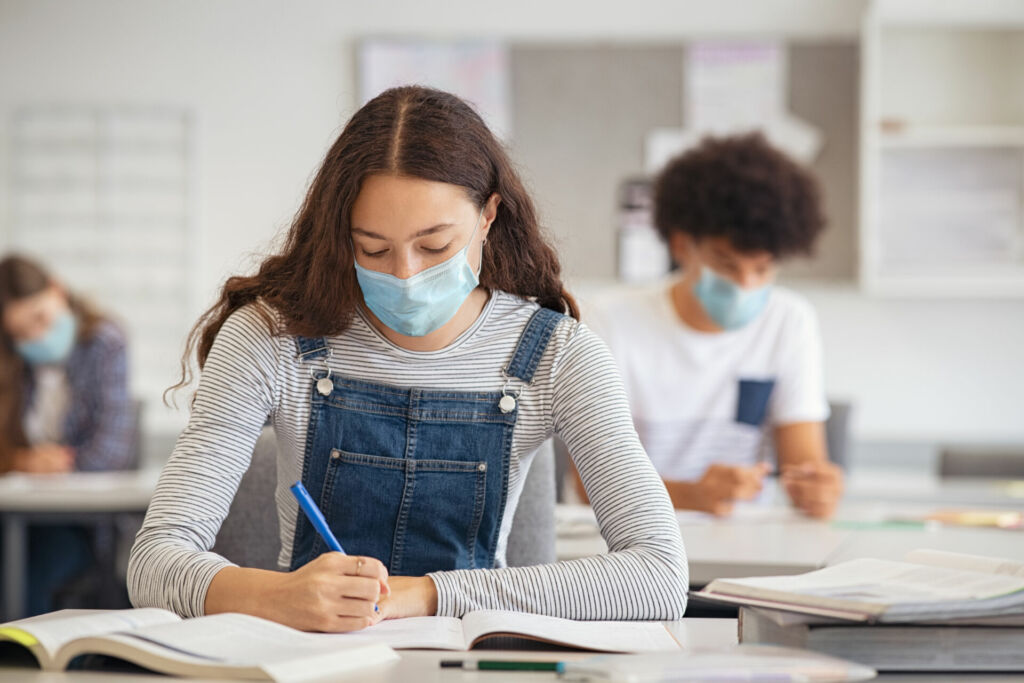 Schülerin sitzt mit Mund-Nasen-Schutz im Klassenzimmer.