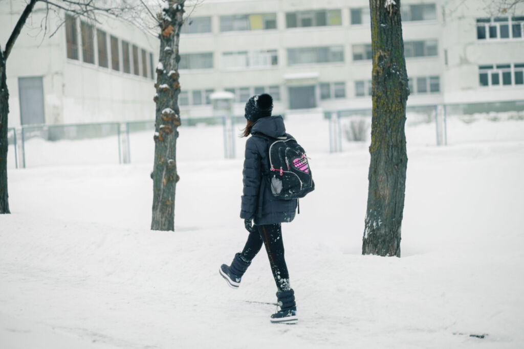 Schüler:in auf dem Weg in die Schule bei Schnee und Glätte.