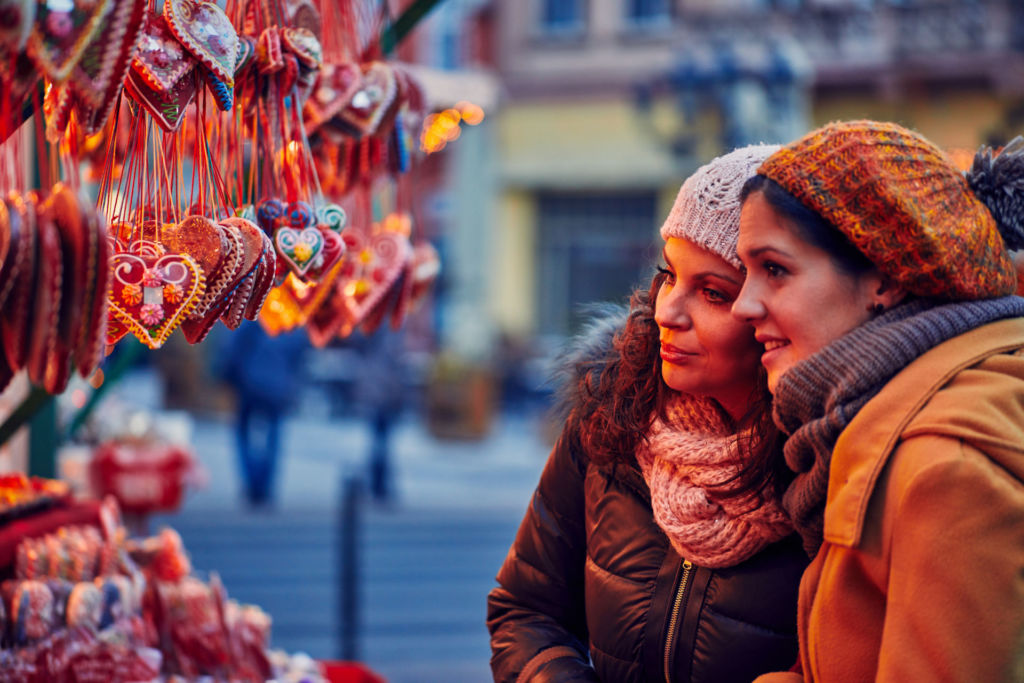 Zwei junge Frauen stehen an einer Weihnachtsmarktbude und suchen sich süßes weihnachtliches Gebäck aus.