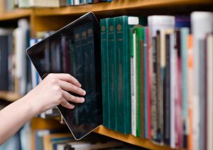 Schüler stellt ein Tablet, als digitales Medium, in ein Bücherregal